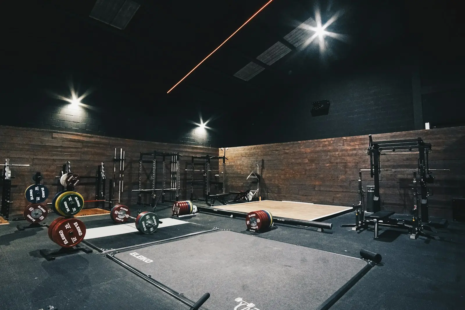 Dark lifting hall with deadlift platforms, loaded bars and wood walls under spot lighting