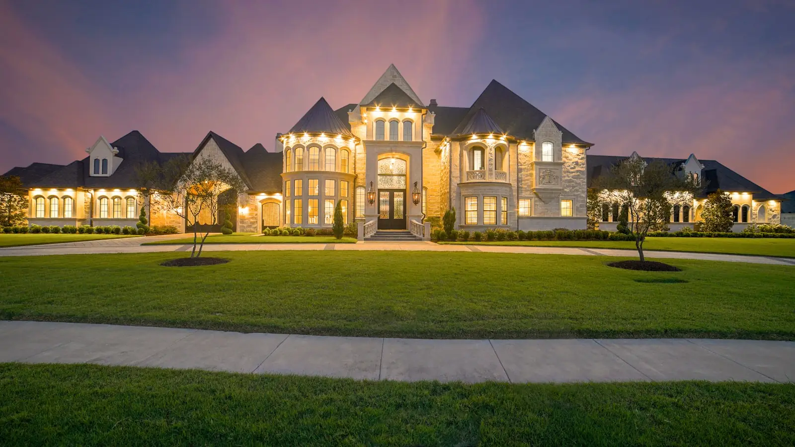 Brick estate home lit warmly at dusk behind a broad lawn