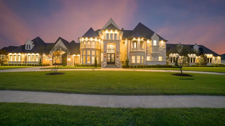 Brick estate at dusk with symmetrical gables and a lit drive