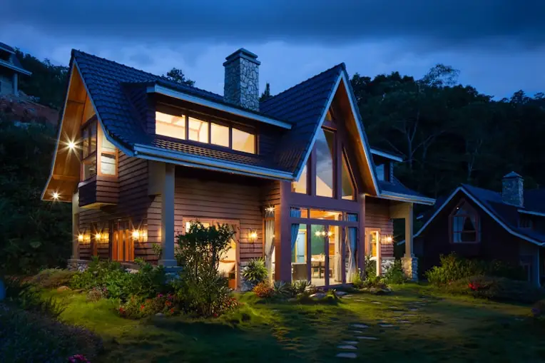 Timber and shingle home glowing at dusk among mature trees