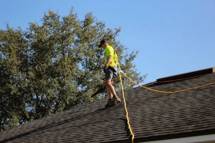 Roofer walking the ridge line of a residential roof with a safety rope
